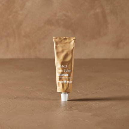 Thrive Tallow Tube of Tinted Sun Balm on a brown textured background