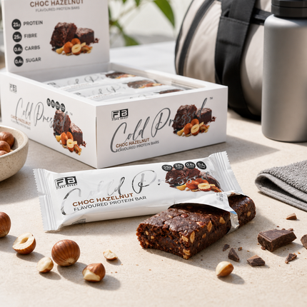Fibre Boost Choc Hazelnut protein bar unwrapped beside the product box, with hazelnuts and chocolate pieces